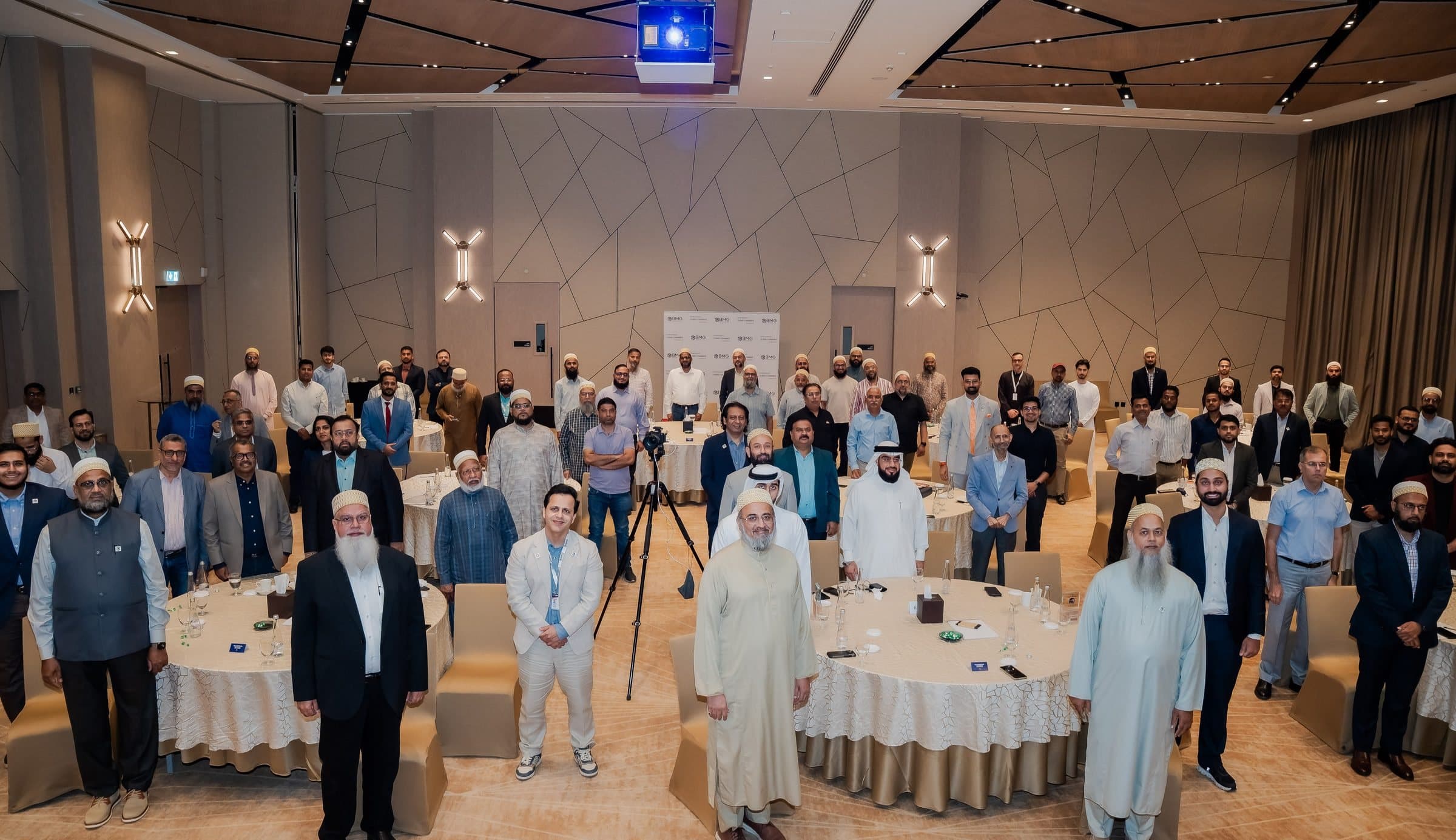 Full room of guests standing among round tables, facing the camera